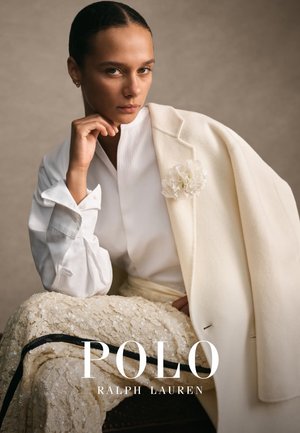 Vit kavaj med blommaccent över en strukturerad krämfärgad kjol. Modellen bär en vit skjortblus med krage, som visar upp ett mjukt tyg och skräddarsydd design.