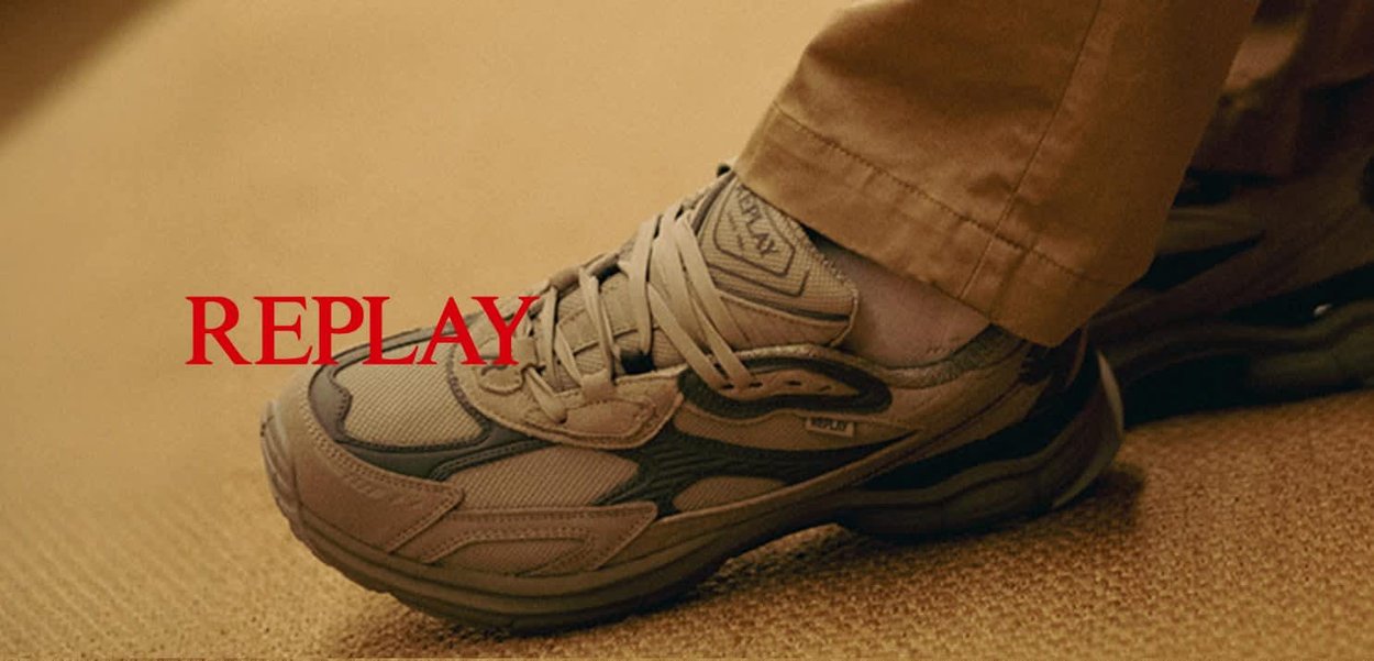 Beige sneakers met textuur overlays, een ondersteunende vorm en zwarte accenten. Veters zichtbaar; logo aan de zijkant. Achtergrond is van neutraal gekleurd vloermateriaal.