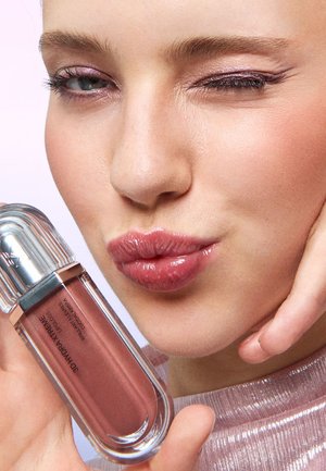 Woman with glossy pink lips winking, holding a tube of rose-colored lip gloss labeled "3D Hydrat Extreme."