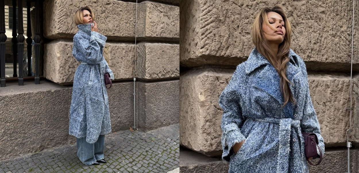 Long manteau surdimensionné en tissu bleu texturé avec une ceinture à la taille, doté de grands revers et de deux boutons, associé à un jean à jambes larges.