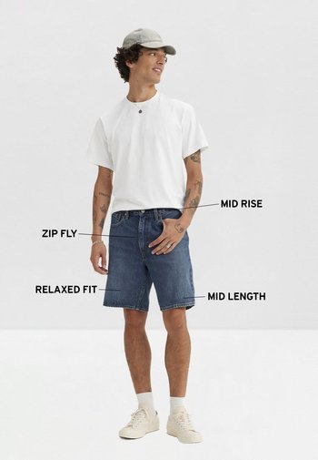 Pantalones cortos de mezclilla de corte relajado, de tiro medio y cierre de cremallera; combinados con una camiseta blanca lisa y zapatillas blancas. Gorra gris claro.