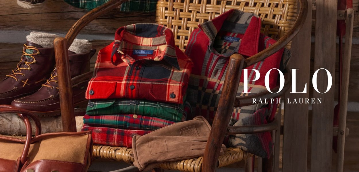 Camice di flanella a quadri in rosso, verde e grigio, impilate su una sedia intrecciata. Stivali in pelle marrone e guanti color camoscio posati nelle vicinanze su una superficie rustica.