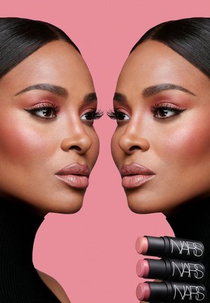 Two faces with dark hair and warm skin tone, showcasing pink makeup. Below, three black stick lip products labeled "NARS." Background is pink.