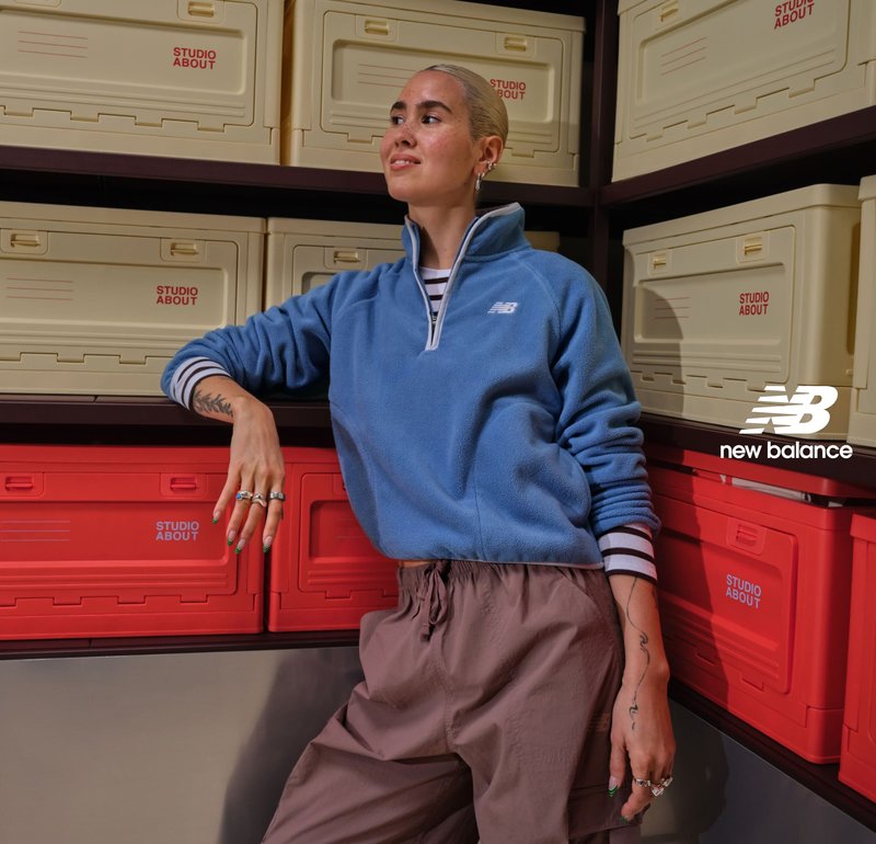 Donna con pile blu e pantaloni marroni appoggiata a scatole di plastica per conservazione rosse e beige con etichetta Studio About.