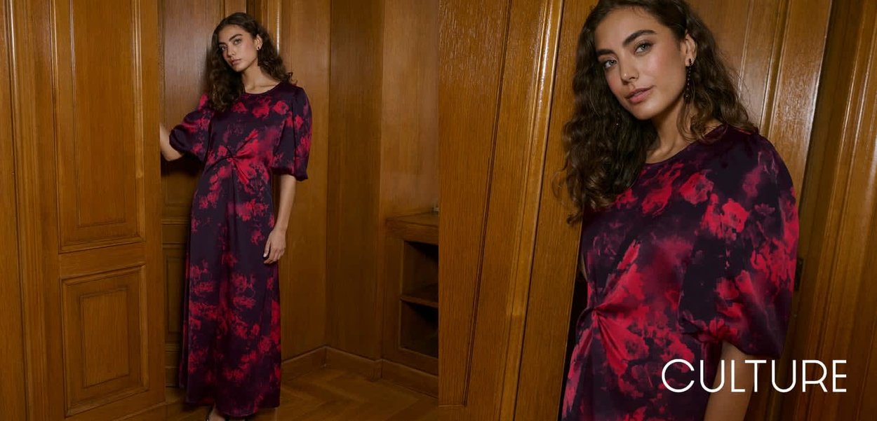 Langes lila Kleid mit roten Blumenmustern, weichem Stoff, kurzen Ärmeln und gerafftem Bund. Vor einem Holz-Hintergrund.