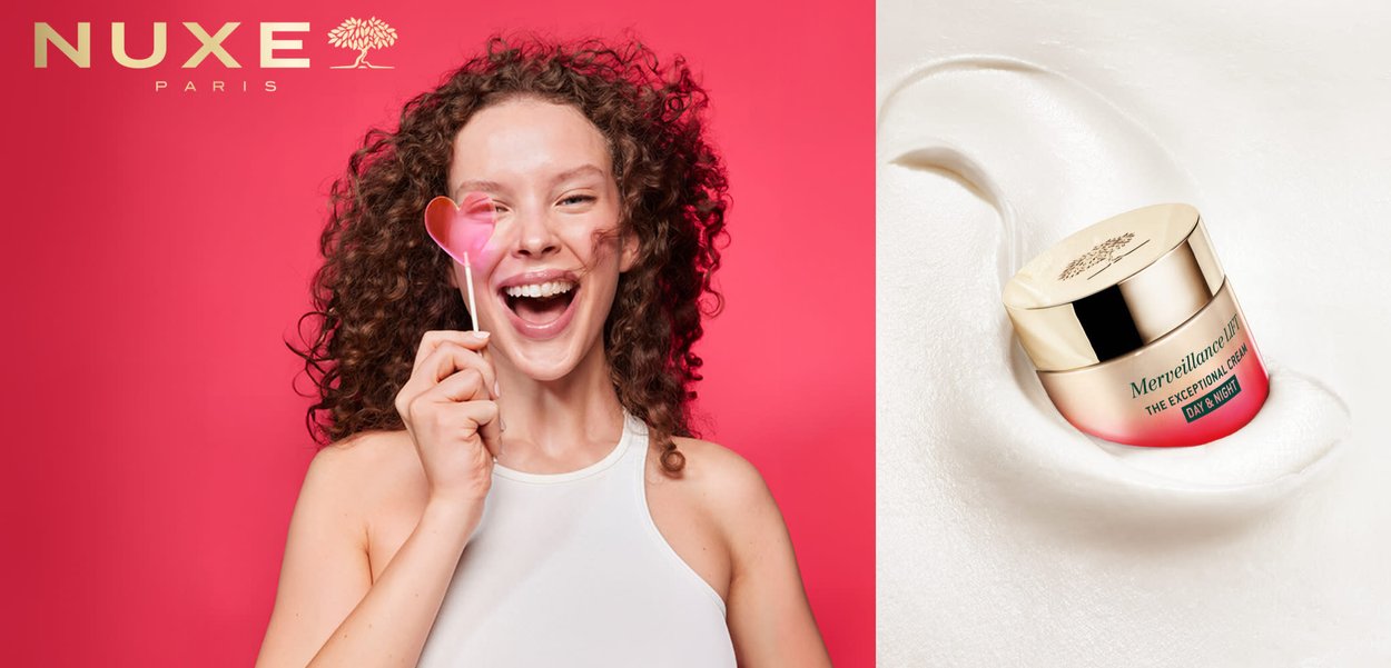 Donna sorridente con capelli ricci che tiene un lecca-lecca rosa a forma di cuore vicino all'occhio accanto al barattolo di crema giorno e notte Nuxe Merveillance Lift.