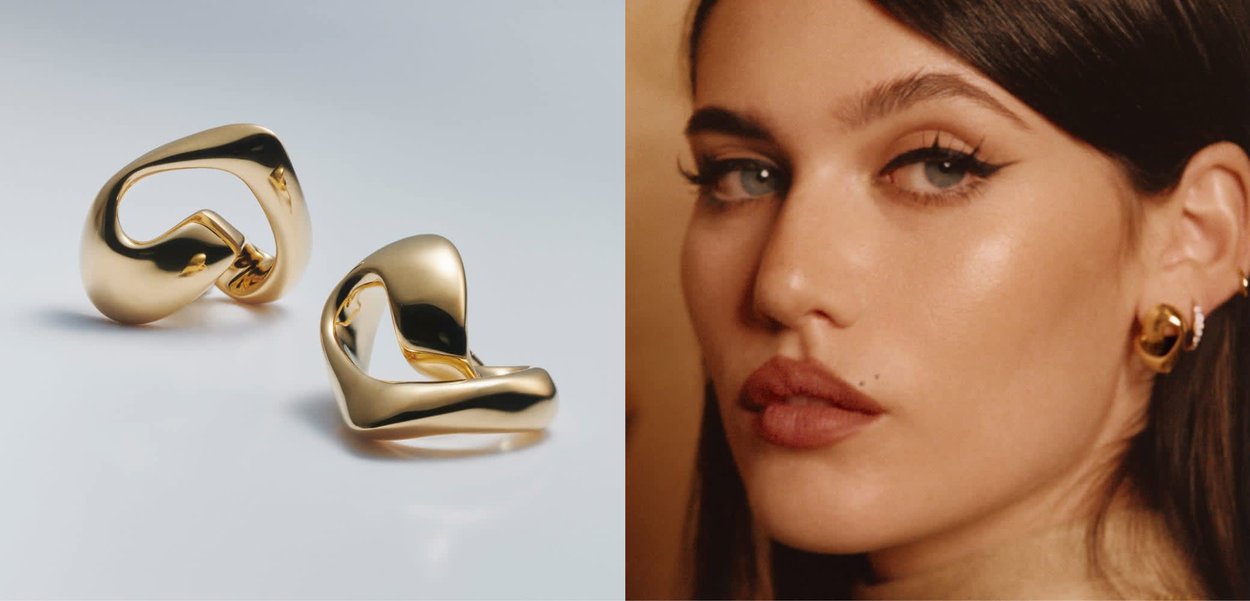 Paar polierte, goldfarbene gedrehte Creolen auf weißem Untergrund, die ihr glattes, reflektierendes und modernes abstraktes Design hervorheben.