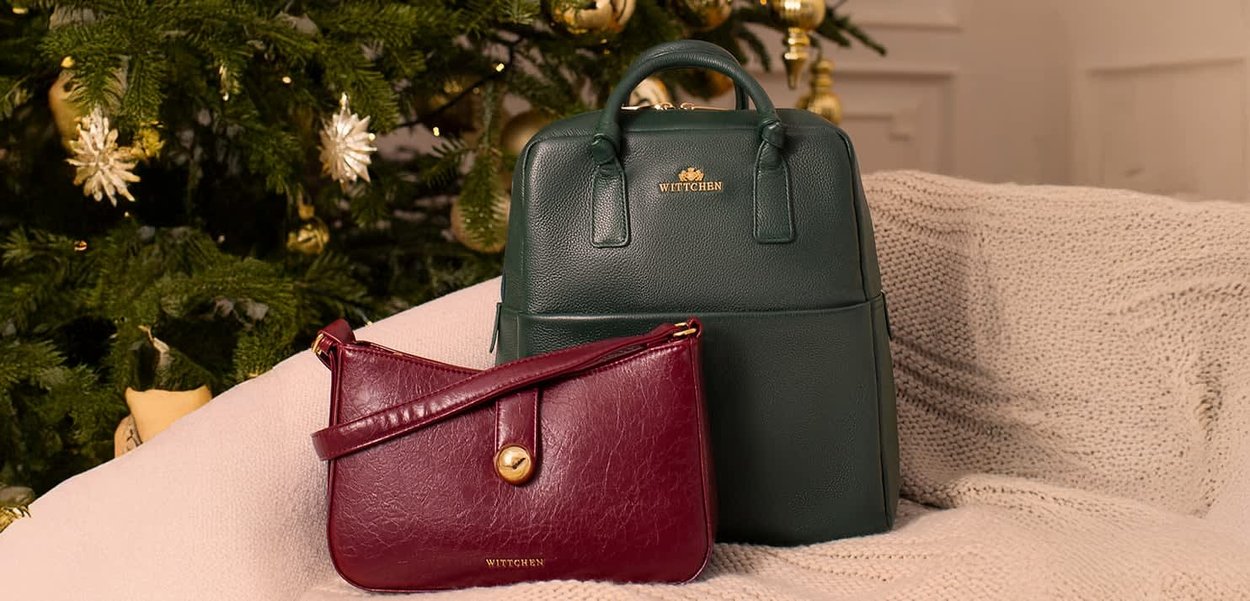 Green leather backpack and burgundy leather crossbody bag on a textured beige blanket, with gold hardware accents and logo details.