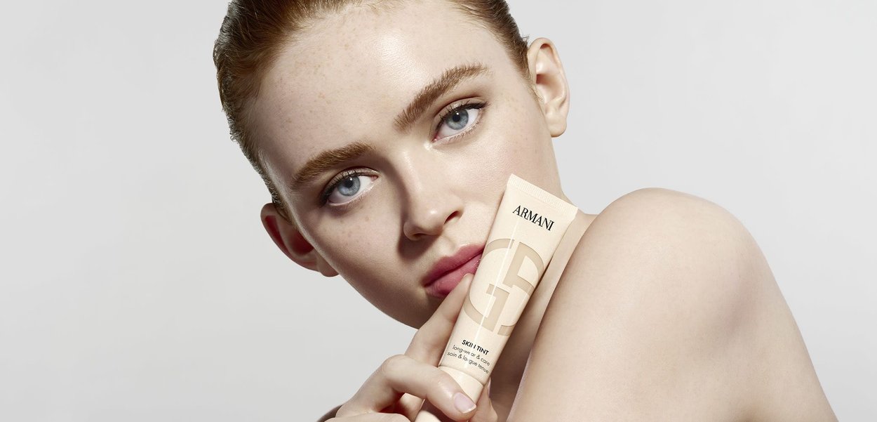 Beige tube of Armani Skintint held against skin, featuring minimalistic design, soft matte finish, and clear text branding.
