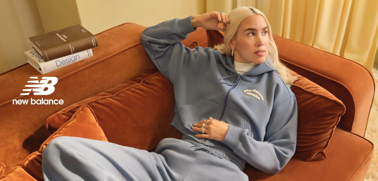 Lichtblauwe hoodie met voorzakken en trekkoord, gecombineerd met bijpassende joggingbroek, tegen een warme oranje sofa. Boeken liggen dichtbij.