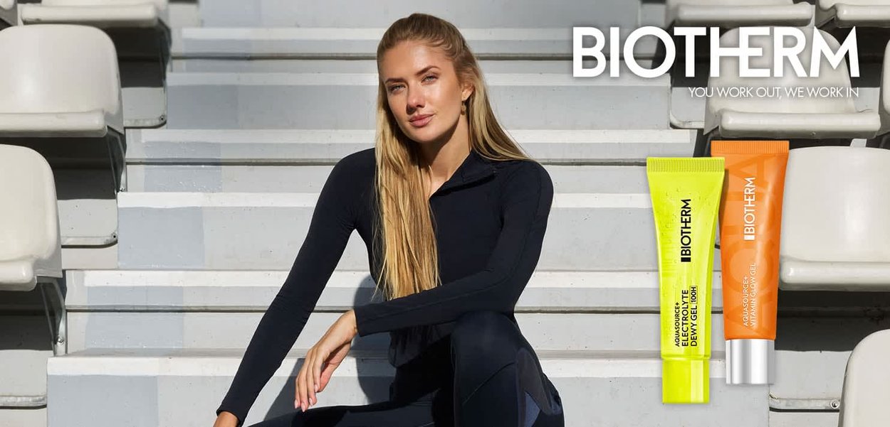 Junge Frau in schwarzer Sportbekleidung sitzt auf Tribünen neben leuchtend gelben und orangefarbenen Biotherm Hautpflege-Tuben.