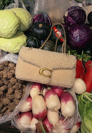 Beige Kunstlammfell-Handtasche mit goldfarbenem Verschluss und Kettenriemen, platziert zwischen verschiedenen Gemüsesorten wie Kohl, Radieschen und Kürbis.