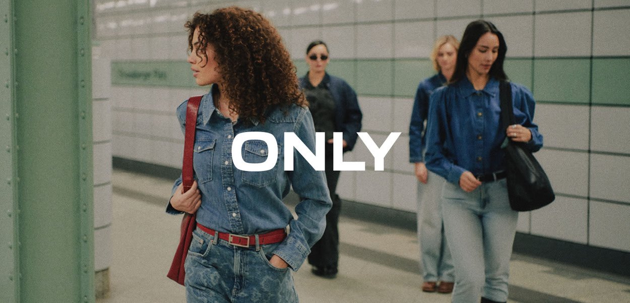 Quattro donne che camminano in un corridoio della metropolitana indossando abiti in denim, con la parola ONLY in lettere bianche e grassetto al centro.