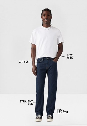 Pantalones vaqueros azul oscuro con tiro bajo, cierre de cremallera y diseño de pierna recta. Presentados en longitud completa y combinados con una camiseta blanca lisa.