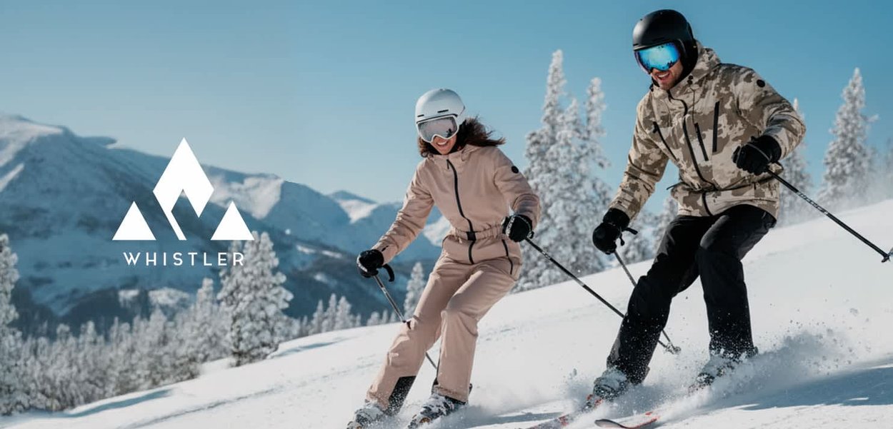 Two skiers on a snowy slope. One wears a light brown ski suit; the other, a camouflage jacket. Both have helmets and goggles.