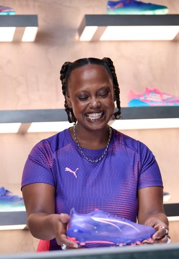 Lila Football-Schuhe mit pinken Akzenten, schlankes Design, leichtes Material, strukturierte Oberfläche, vor einem beleuchteten Regalhintergrund präsentiert.