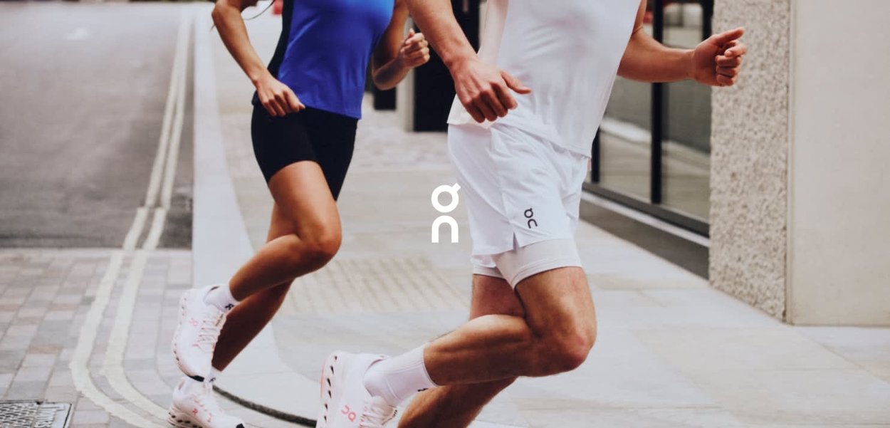 Deux coureurs en tenue de sport courent dans une rue de la ville. La femme porte un haut bleu et un short noir ; l'homme est en chemise blanche et en short.