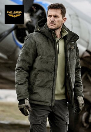 Pikowana kurtka w ciemnooliwkowym kolorze z odpinanym kapturem, noszona na jasnozielonym topie zapinanym na zamek. Charakteryzuje się fakturowanym wykończeniem i praktycznymi kieszeniami.