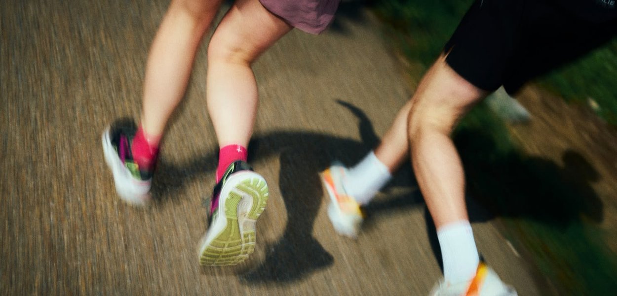 Zwei Personen laufen auf einem gepflasterten Weg, tragen Sportschuhe, Shorts und Socken, aufgenommen von hinten bei Dämmerung im Freien.