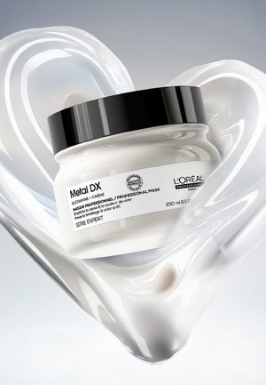 L’Oréal Metal DX professionelle Haarmaske im Glas mit schwarzem Deckel, umgeben von einer herzförmigen Spirale aus weißer Creme.