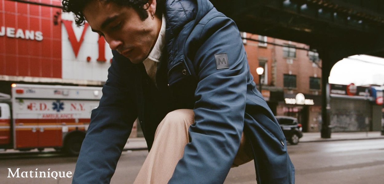 Junger Mann in blauem Jacke hockt auf der Straße in der Stadt nahe einem Rettungswagen und einem roten Geschäft unter einer Autobahnbrücke.