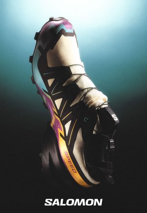Zapatilla Salomon Speedcross 3, con una parte superior en color crema y detalles en negro y púrpura, suela texturizada, diseño robusto y cordones para un ajuste seguro.
