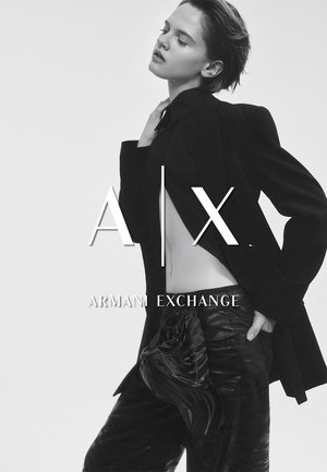 Schwarzer taillierter Blazer über einem eng anliegenden Oberteil, kombiniert mit glänzenden schwarzen Hosen. Enthält eine strukturierte Tasche, die das Outfit akzentuiert. Monochromes Farbschema.