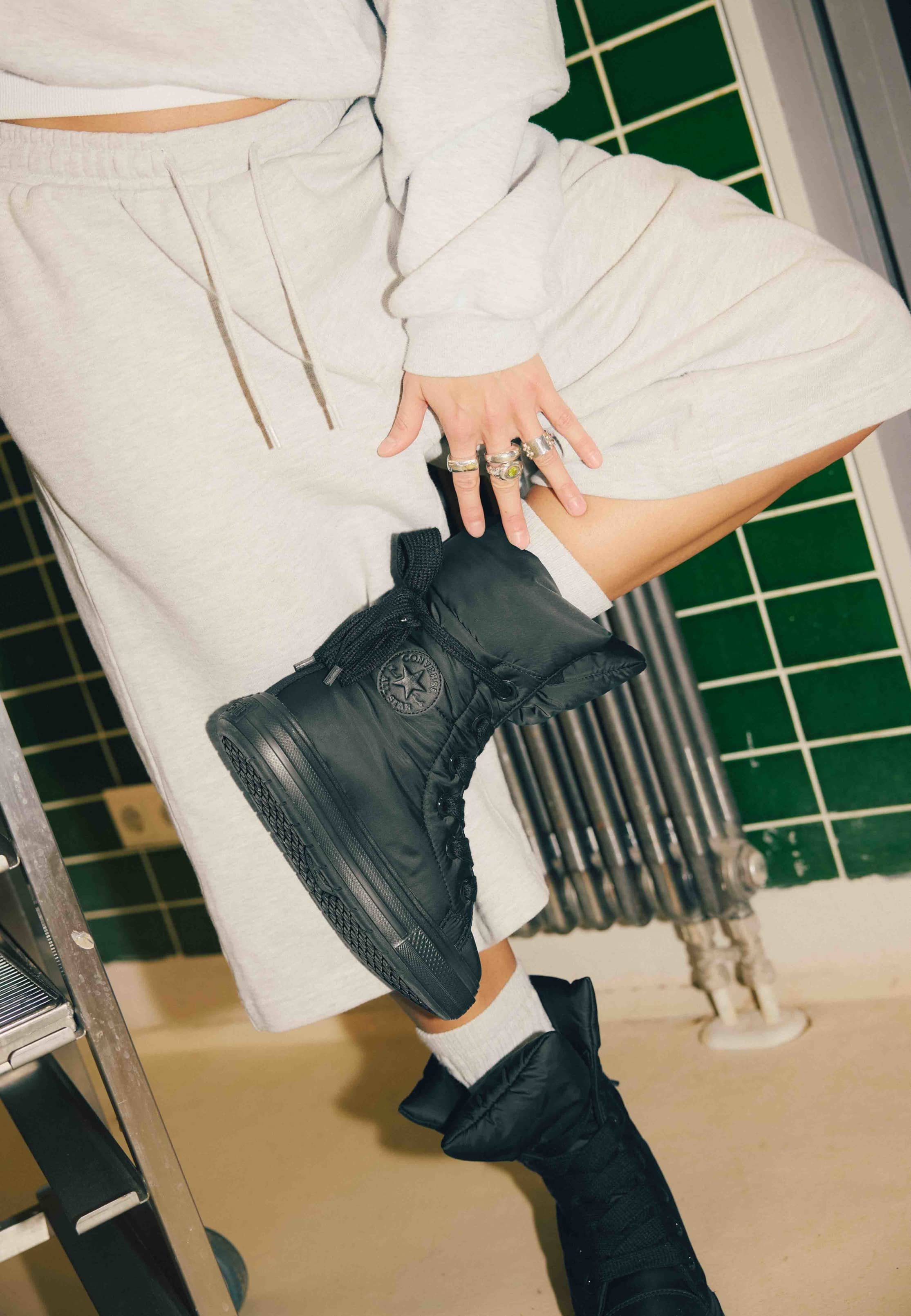 Botas negras acolchadas de diseño alto, con suela dentada y cierre de cordones, combinadas con un conjunto corto gris y calcetines blancos hasta el tobillo.