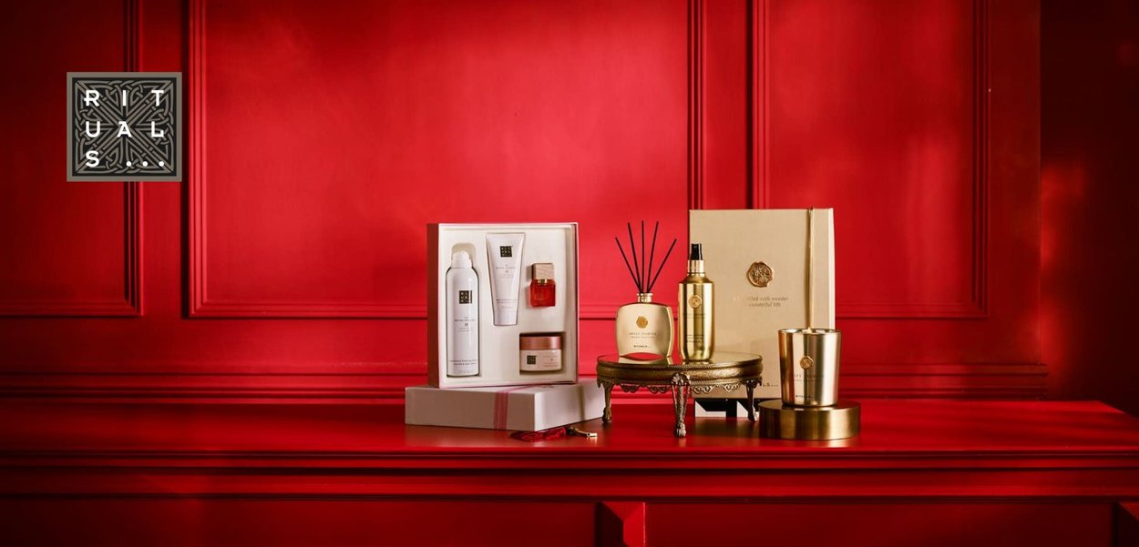Sett med luksuriøse hudpleie- og duftprodukter vist på en rød overflate; inkluderer hvite flasker, gullaksenter og en kremfarget eske.