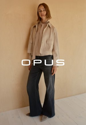 Beige cropped jas met twee voorkruiden, gecombineerd met donker flare jeans. Gekleed met een lichte top met een halsband en grijze puntige schoenen.