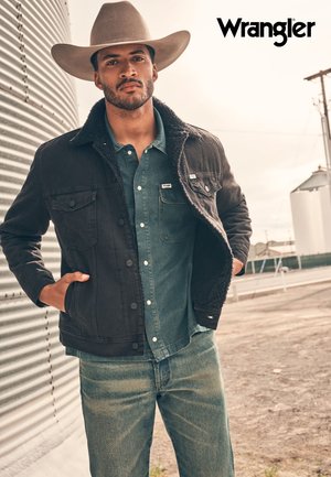 Svart denimjakke med fôr av pels over en blå denimskjorte, paret med lyseblå jeans. En bredbremmet lyshatt fullfører antrekket.