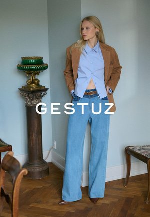Tan suede blazer over a light blue button-up shirt, paired with wide-leg light blue jeans. Brown leather belt and pointed toe shoes.