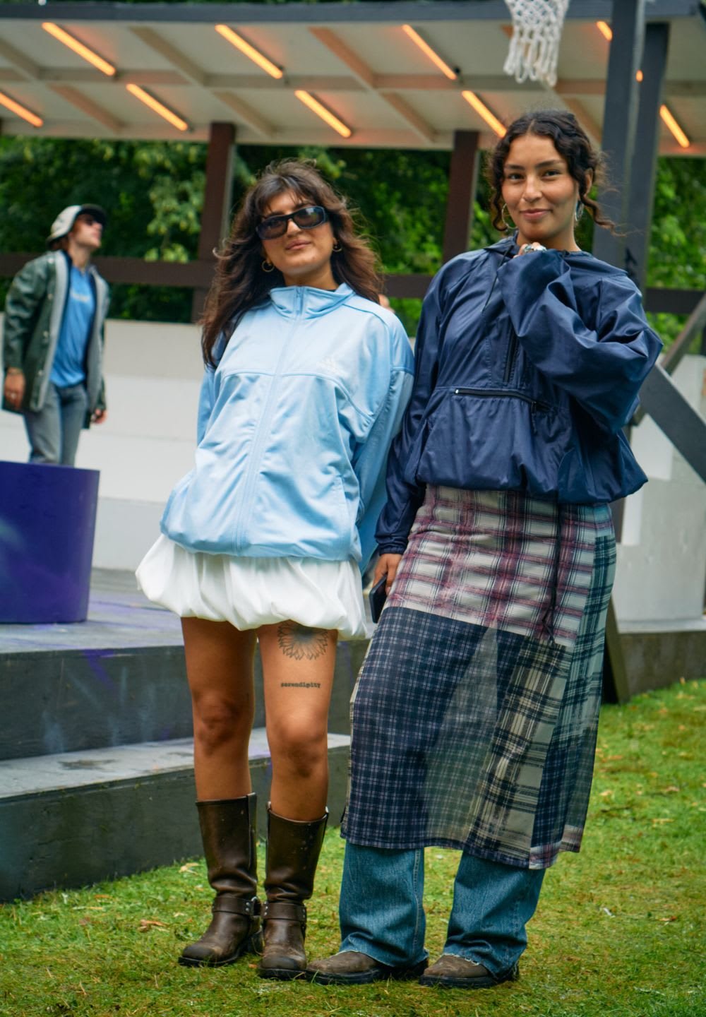 Två personer står sida vid sida. Den ena har på sig en ljusblå jacka och vit kjol, medan den andra har på sig en marinblå jacka och rutiga kjolar över jeans.