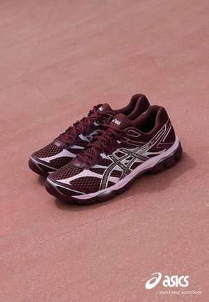 Et par bordeaux og lyserøde ASICS Gel-Contend 7 løbesko placeret på en rød tekstureret overflade med ASICS-logo og slogan i nederste hjørne.