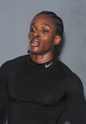 Camiseta deportiva ajustada de manga larga negra con cuello alto y logo reflectante de Nike. El modelo tiene el cabello trenzado y el rostro brillante.