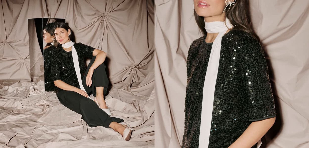 Musta paljettipusero lyhyillä hihoilla, yhdistetty mustiin housuihin. Valkoinen huivi korostaa pääntietä. Yksinkertaiset valkoiset kengät viimeistelevät asun.