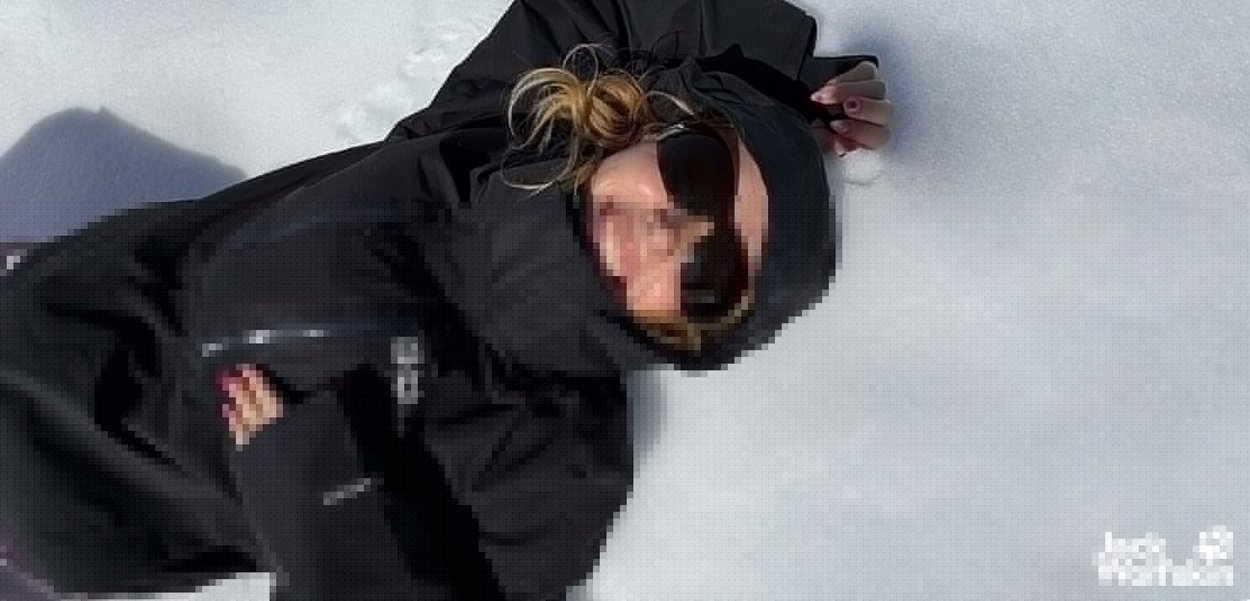 Zwarte geïsoleerde jas met hoge kraag, ritsdetails en zachte textuur. Zonnebril weerkaatst licht tegen een sneeuwachtige achtergrond.