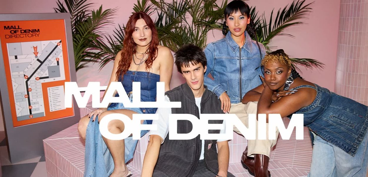 Vier diverse jonge volwassenen in denim outfits poseren in een roze getegelde winkelcentrum met een winkelgids en groenvoorzieningen op de achtergrond.