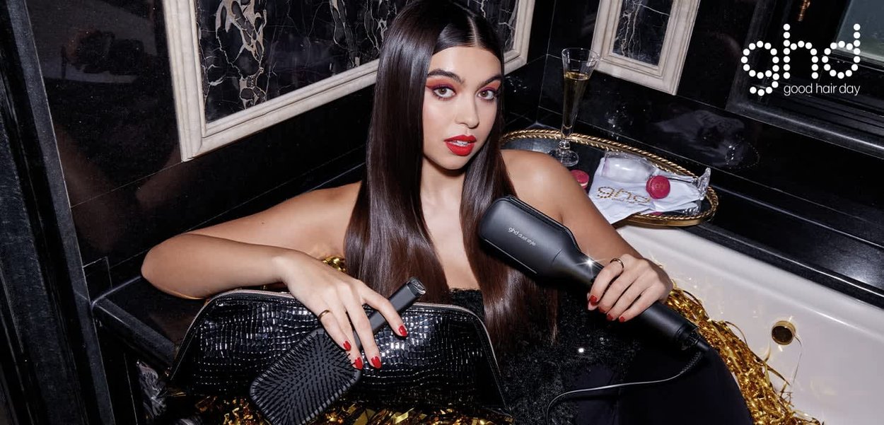 Svart hårfön och borste på kanten av ett badkar, med gyllene accenter och blanka svarta kakelplattor. Modellen håller en hårfön och visar upp sitt släta, långa hår.