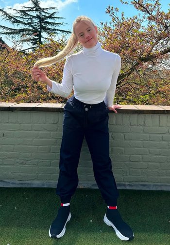 Vit polokrage topp ihop med marinblå joggerbyxor; svarta slip-on skor med röda och vita accenter; utomhusmiljö med grönska i bakgrunden.