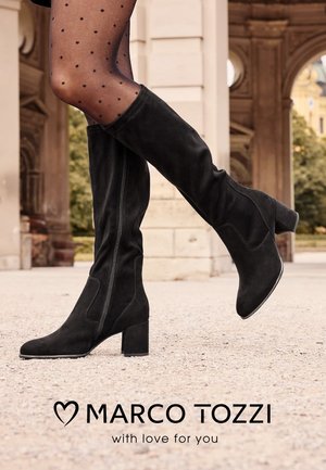 Black suede knee-high boots with a block heel, featuring a side zipper and a smooth texture, set against a light stone surface.
