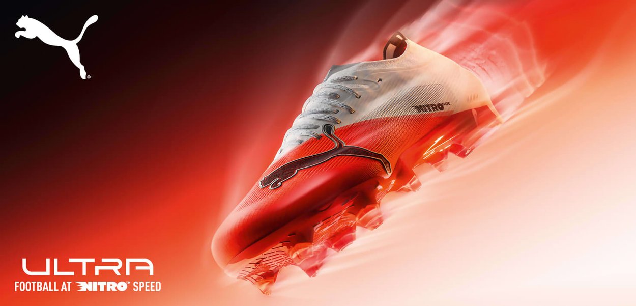 Roter und weißer Puma Fußballschuh mit schwarzem Logo, leuchtenden Stollen, aus einem Winkel auf rotem verschwommenem Hintergrund mit Geschwindigkeitseffekten gezeigt.