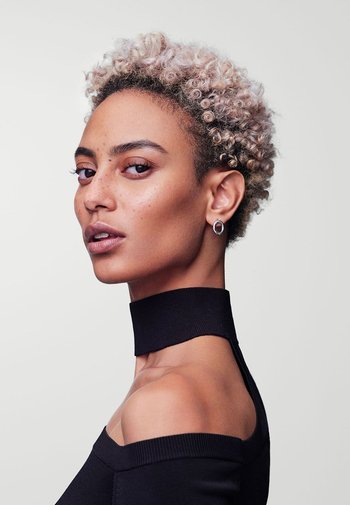 Black off-shoulder top with a chunky neck, featuring a textured knit. Light curly hair, pierced ear with a silver hoop earring.