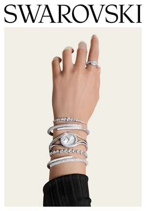 Srebrne bransoletki i zegarek, misternie zaprojektowane z błyszczącymi kryształami i teksturowanymi paskami, prezentowane na dłoni z czarnym mankietem.