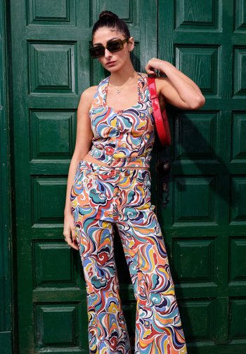 Šaren, uzorak dvoslojni komplet s bezrukavom majicom i hlačama širenog kroja. Materijal izgleda lagano. Dodaci uključuju crvenu torbu.