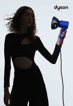 Asciugacapelli Dyson con accenti blu e rossi, caratterizzato da un design unico e una presa testurizzata. Il modello tiene il dispositivo contro uno sfondo chiaro.