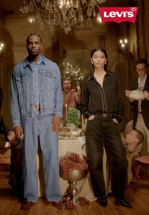 Twee modellen dragen Levi's-kleding: een spijkerjack en spijkerbroek voor de één, een zwart overhemd met knopen en donkere jeans voor de ander. Op de achtergrond is een eetscene te zien.
