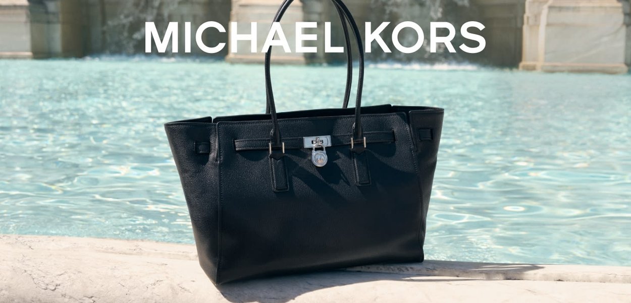 Borsa tote nera in pelle con due manici, un meccanismo di chiusura in argento e un design minimalista. Ambientata contro uno sfondo acquamarina.