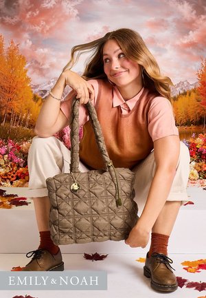 Borsa trapuntata marrone con due manici intrecciati, decorata con un charm ornamentale, su uno sfondo autunnale colorato.