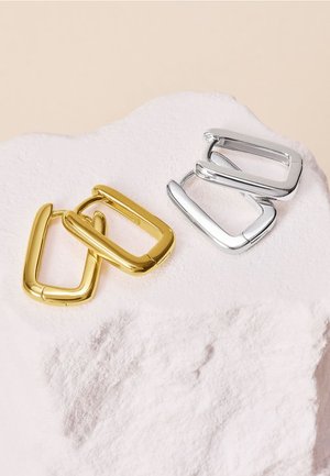 Due fibbie metalliche di forma quadrata: una dorata e una argentata. Hanno una superficie liscia e lucida con bordi arrotondati, posizionate su uno sfondo chiaro e testurizzato.